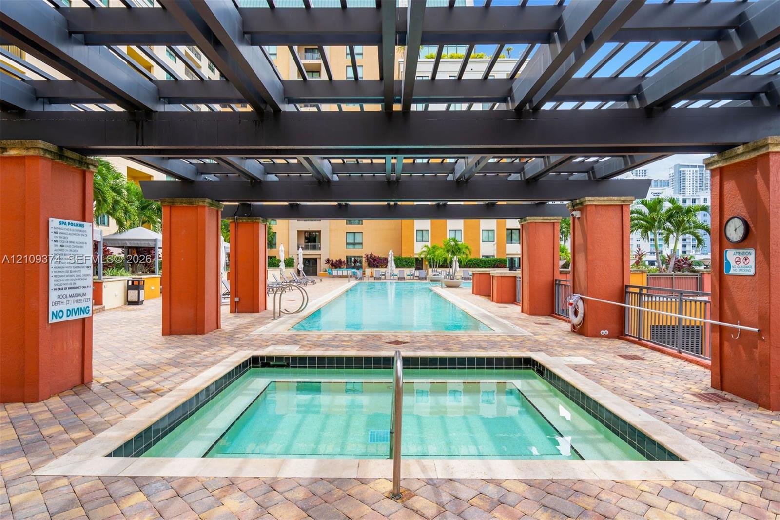 Outdoor spa and swimming pool area featuring a large overhead pergola, stone paver decking, and stucco-finished columns