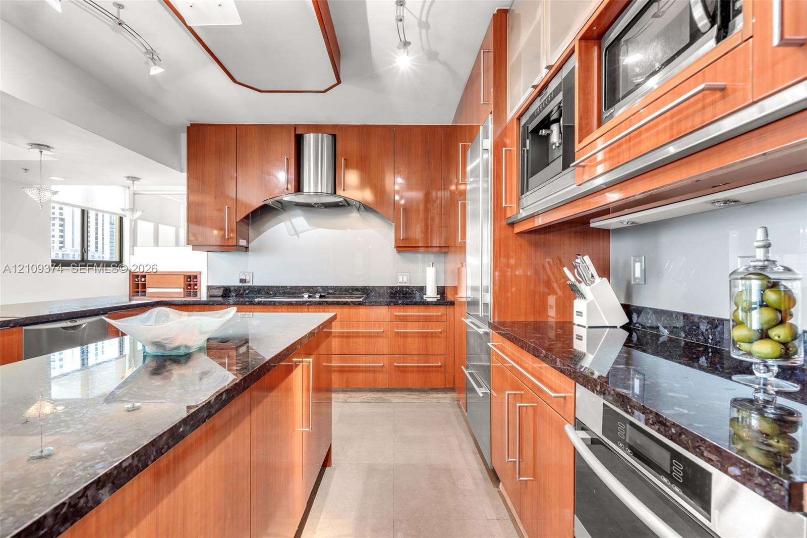 Kitchen featuring warm-toned cabinetry, expansive stone countertops, built-in stainless steel appliances, a professional-style range hood, and track lighting