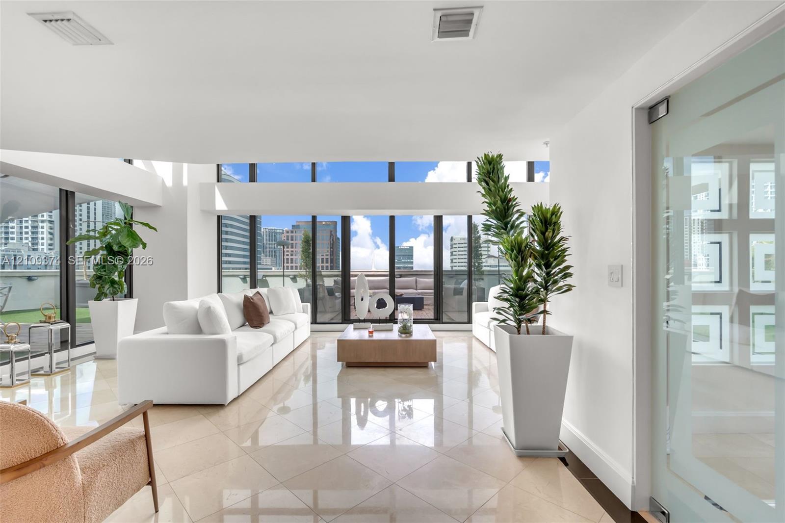 Expansive living area featuring floor-to-ceiling windows, polished stone flooring, and a glass-panel door Expansive living area featuring floor-to-ceiling windows, polished stone flooring, and a glass-panel door