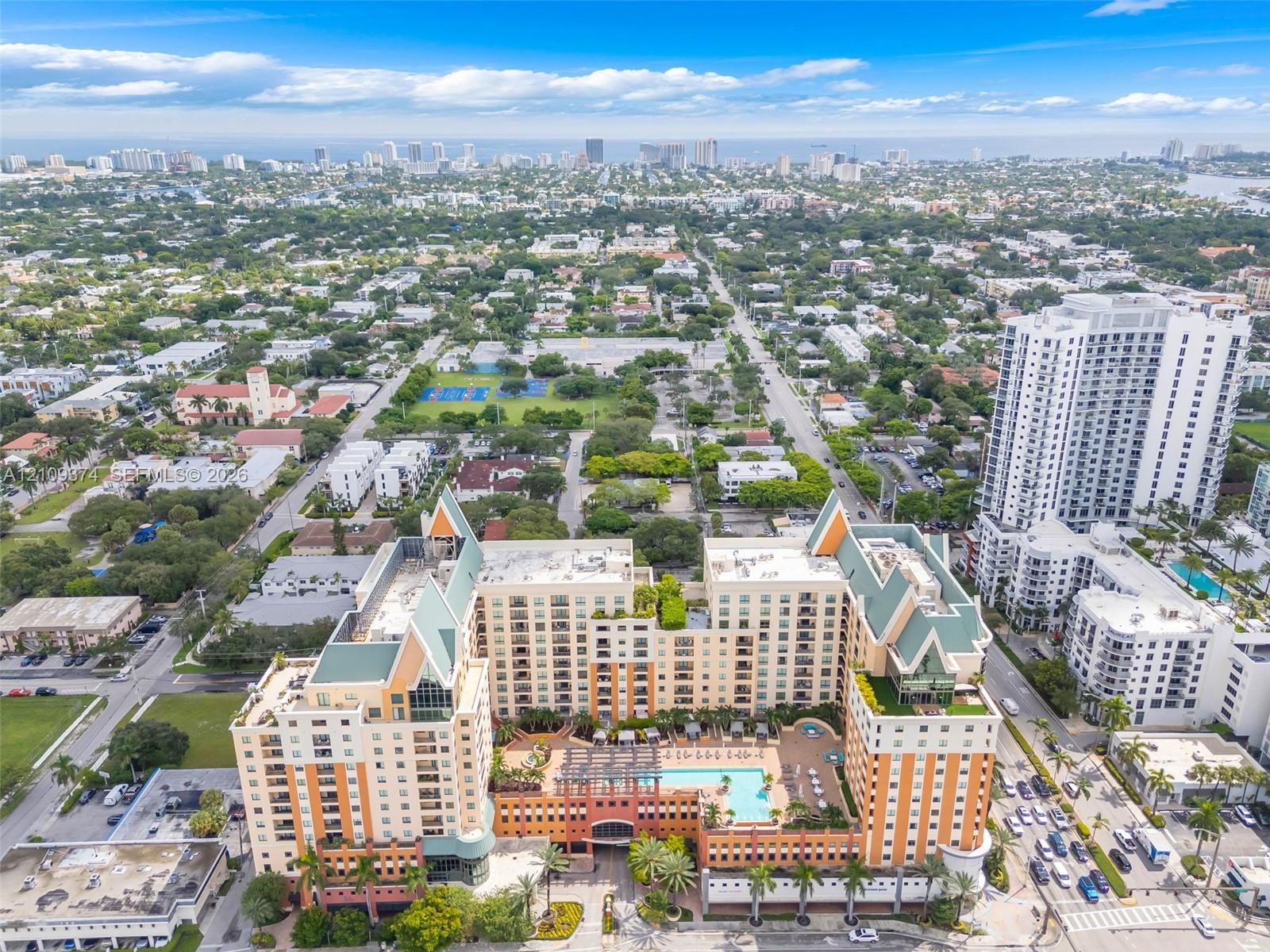 Aerial perspective of a multi-story residential complex featuring a central outdoor swimming pool, terracotta-toned facade, decorative pitched roofing, and expansive terrace levels