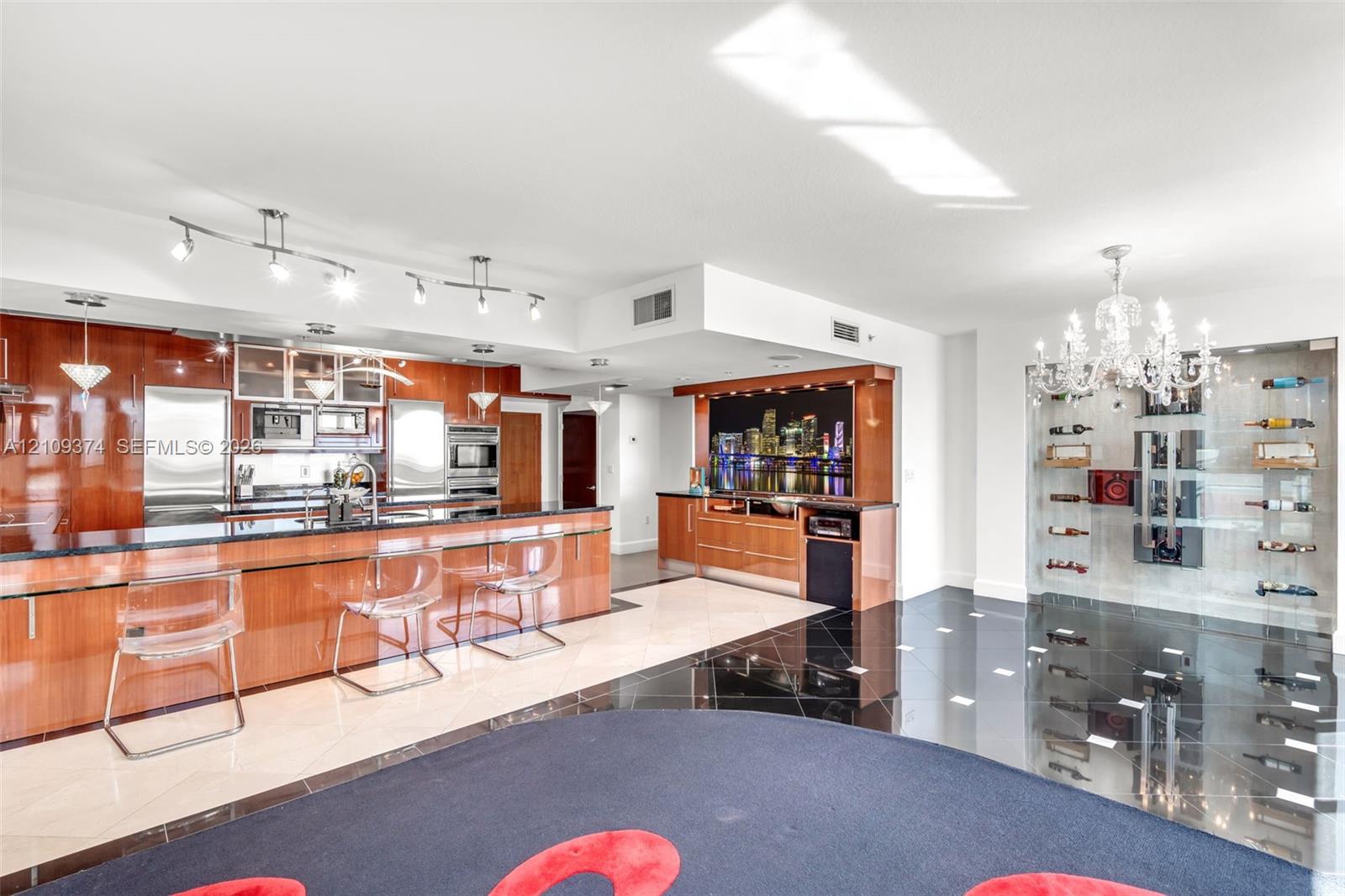 Modern kitchen featuring high-gloss cabinetry, dark stone countertops, built-in stainless steel appliances, a recessed wet bar, and a floor-to-ceiling glass-enclosed wine display