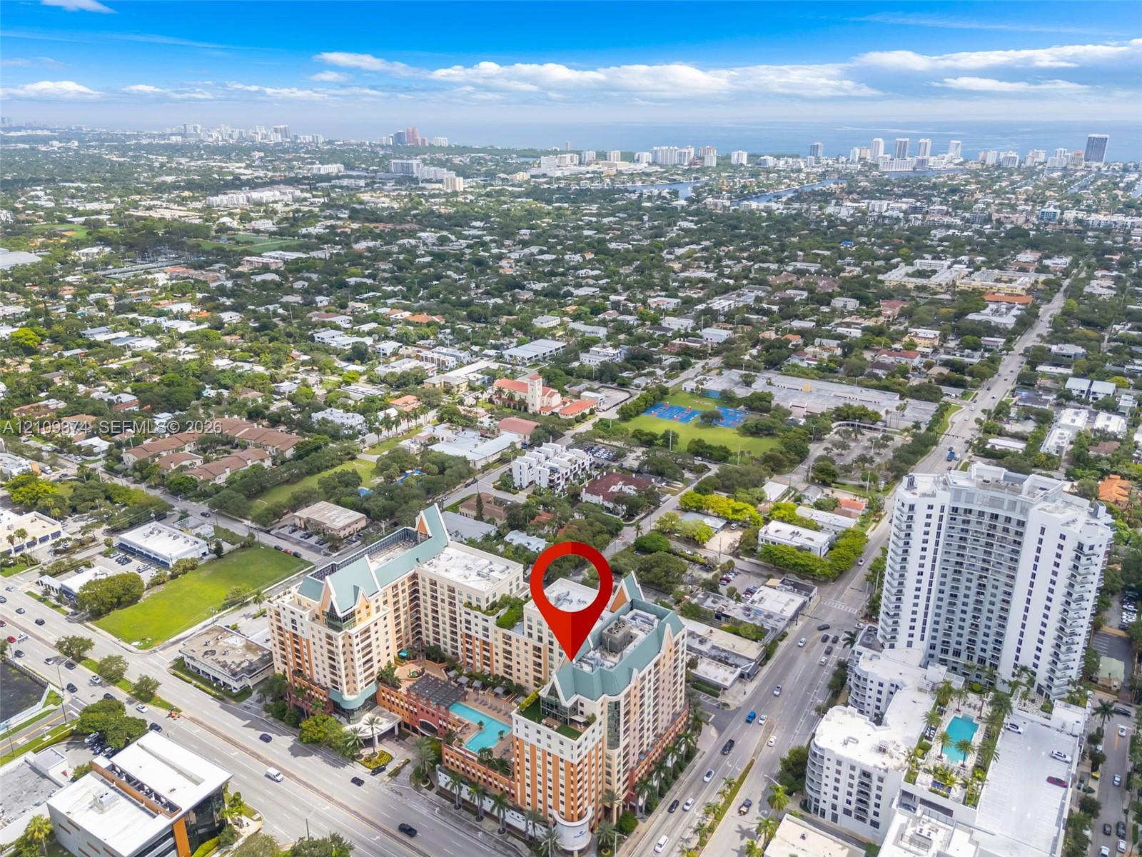 Aerial perspective of a multi-story residential building featuring a sprawling outdoor pool deck, terraced balconies, and a distinctive peaked roofline