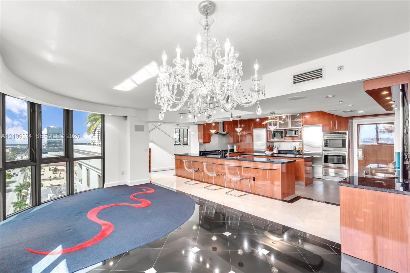 Kitchen featuring high-gloss wood cabinetry, dark stone countertops, built-in stainless steel appliances, a large center island, and an ornate crystal chandelier