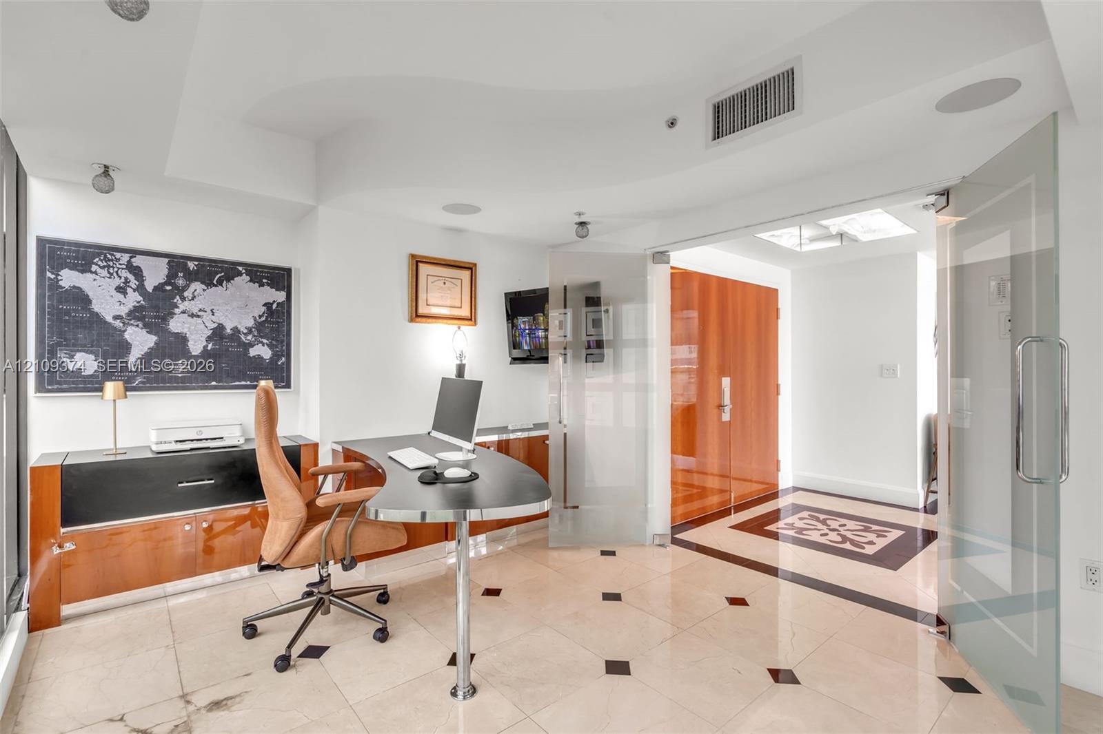 Light-filled room featuring large-format stone flooring with decorative inlay, custom wood-finish built-in cabinetry, frosted glass pivot entry doors, and recessed ceiling lighting