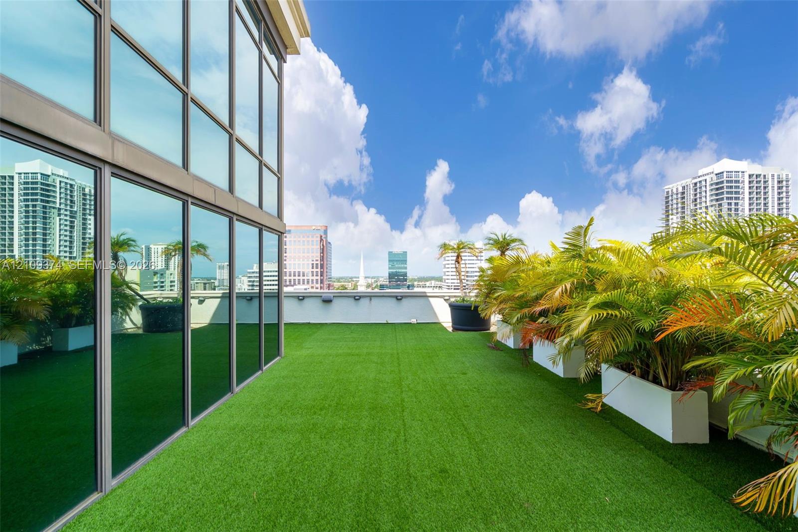 Expansive outdoor terrace featuring synthetic turf flooring, floor-to-ceiling glass paneling, and built-in rectangular planters