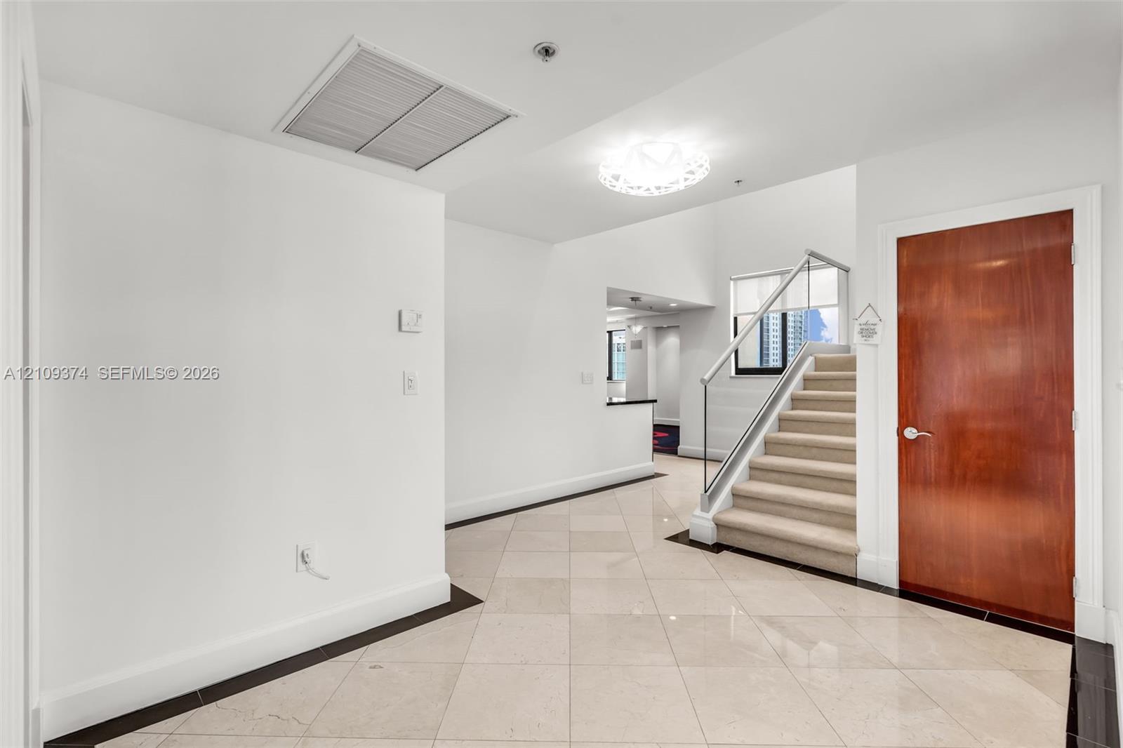 Entryway featuring large-format diagonal tile flooring, a solid wood-finish entry door, a staircase with a glass panel railing, and a decorative circular ceiling light fixture