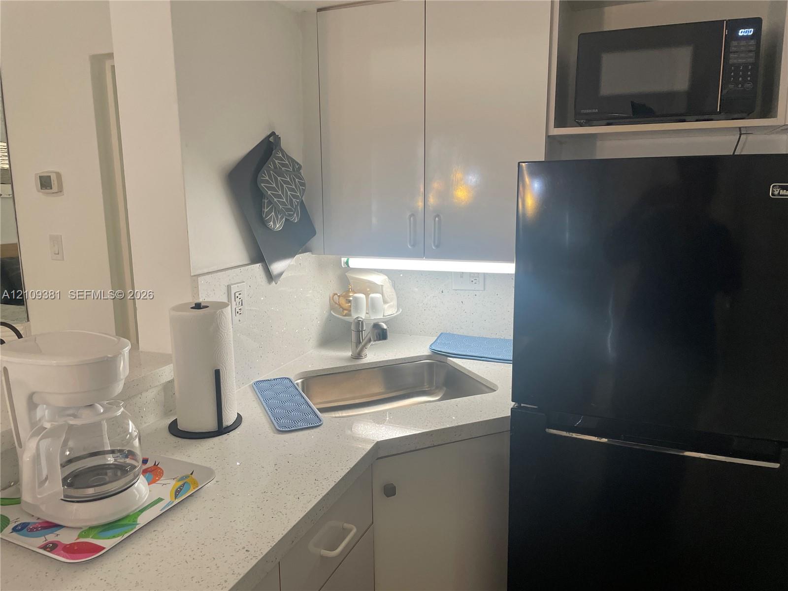 Kitchen area featuring a quartz countertop peninsula, white cabinetry, a built-in microwave, a stainless steel sink, and light-toned tile flooring