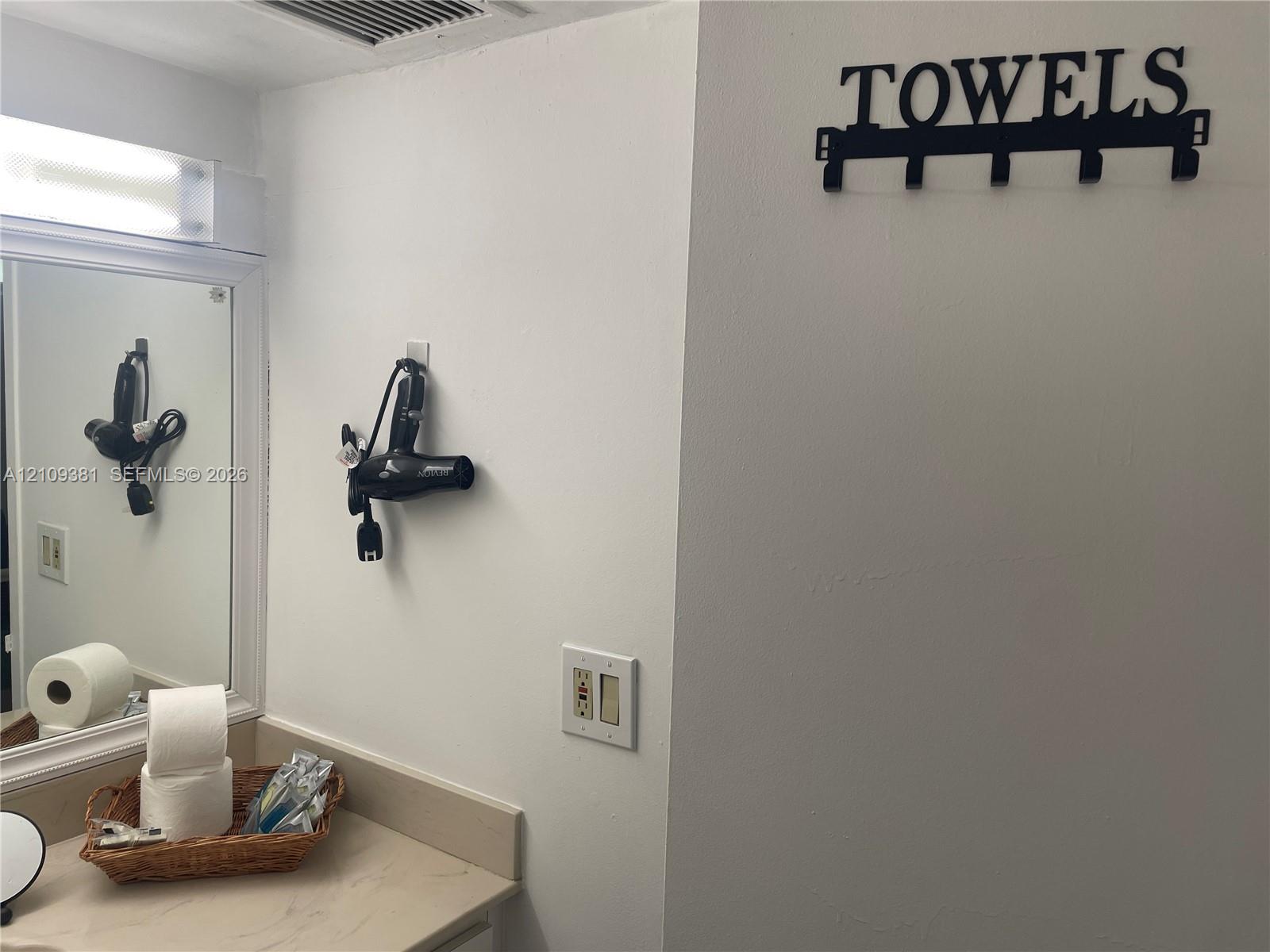 Bathroom featuring a vanity with a solid-surface integrated sink, white cabinetry, a large wall mirror, and white tile wall accents