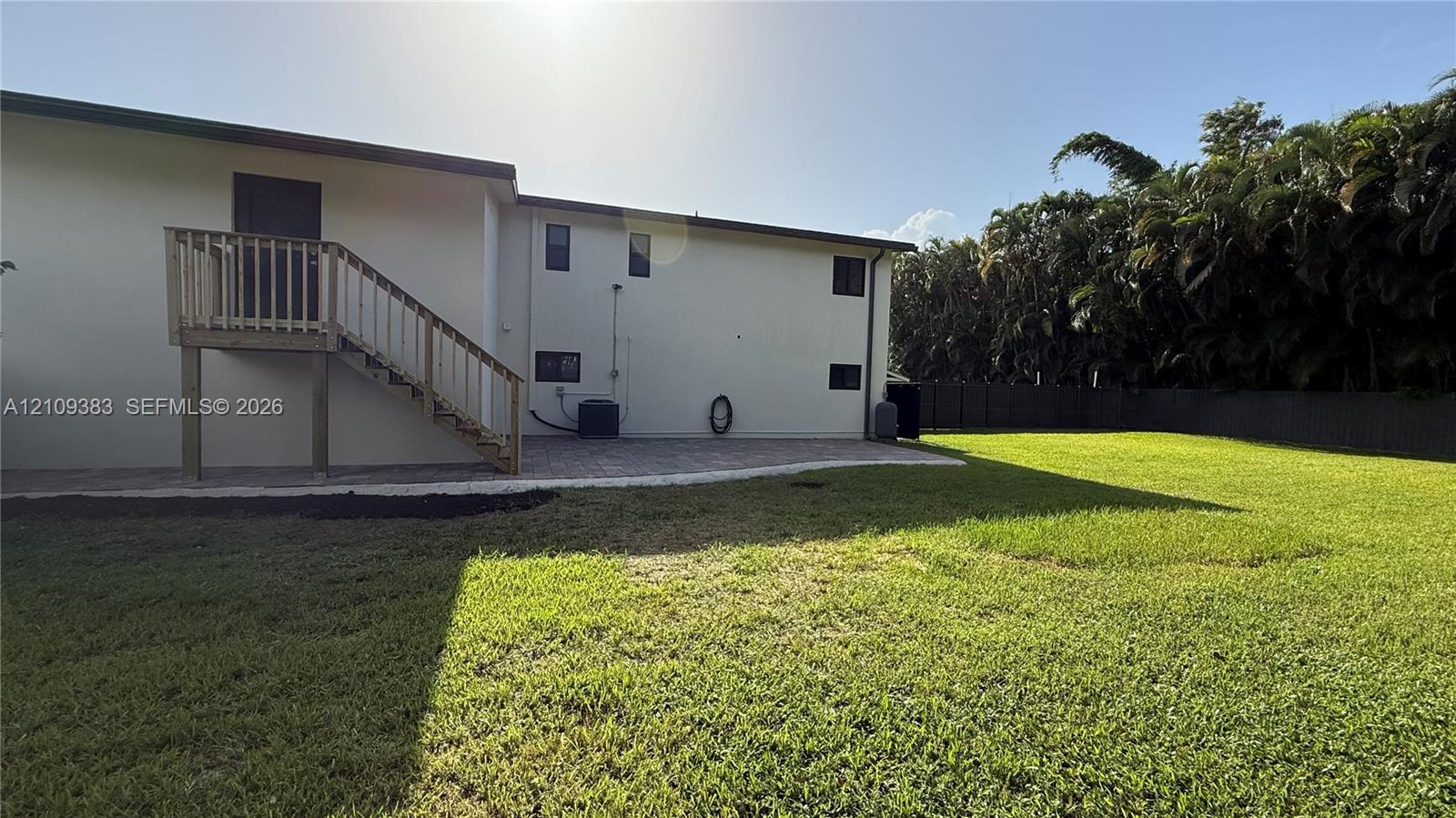 Backyard featuring an expansive lawn, paver patio, wood-railing exterior staircase, and perimeter fencing