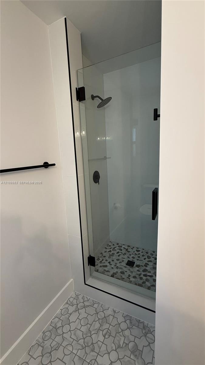 Walk-in shower featuring a frameless glass door, matte black fixtures, pebble tile flooring, and geometric pattern floor tile