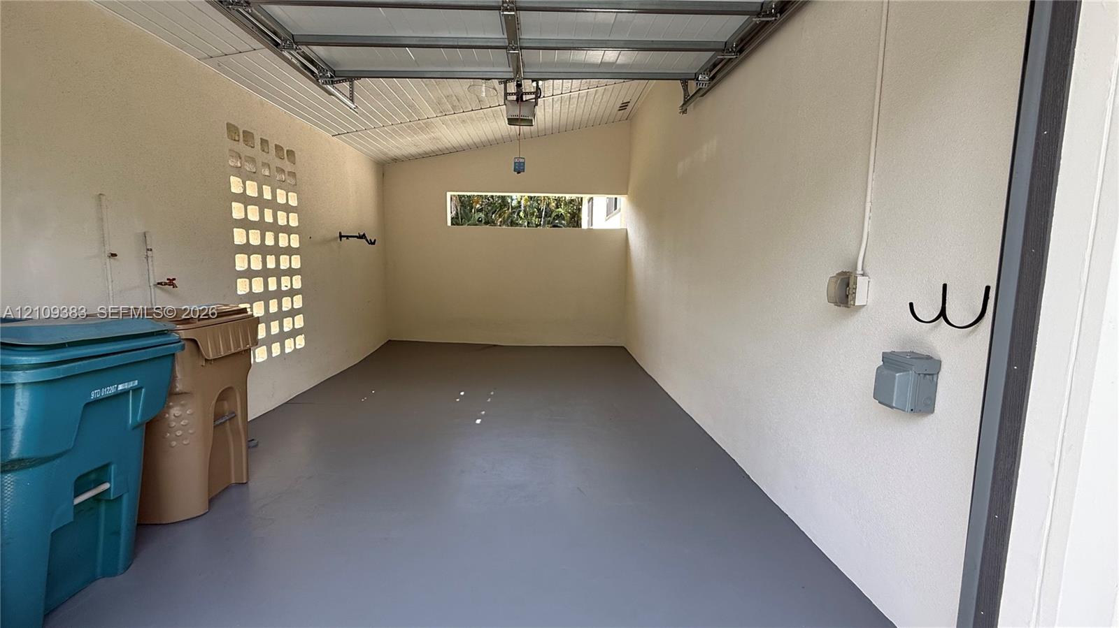 Enclosed garage featuring a concrete floor, textured wall finish, integrated glass block masonry, and horizontal clerestory window