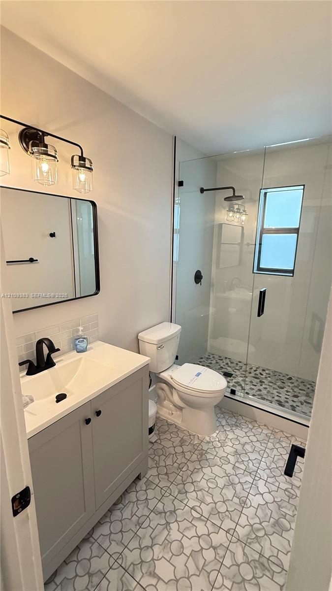 Bathroom featuring a gray vanity with a white countertop, matte black fixtures, a walk-in shower with a glass enclosure, and patterned tile flooring