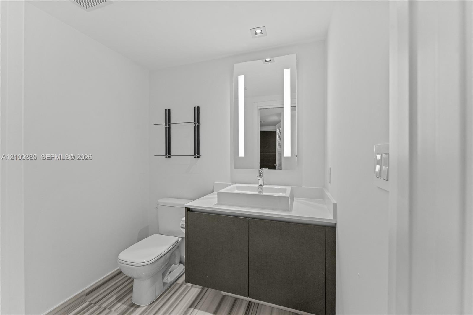 Wall-mounted vanity with a rectangular vessel sink and countertop, backlit rectangular mirror, and glass wall shelving