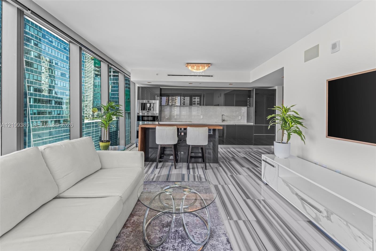 Floor-to-ceiling windows, high-gloss cabinetry, stone-patterned tile flooring, integrated kitchen appliances, and a kitchen island with a wood-finish countertop