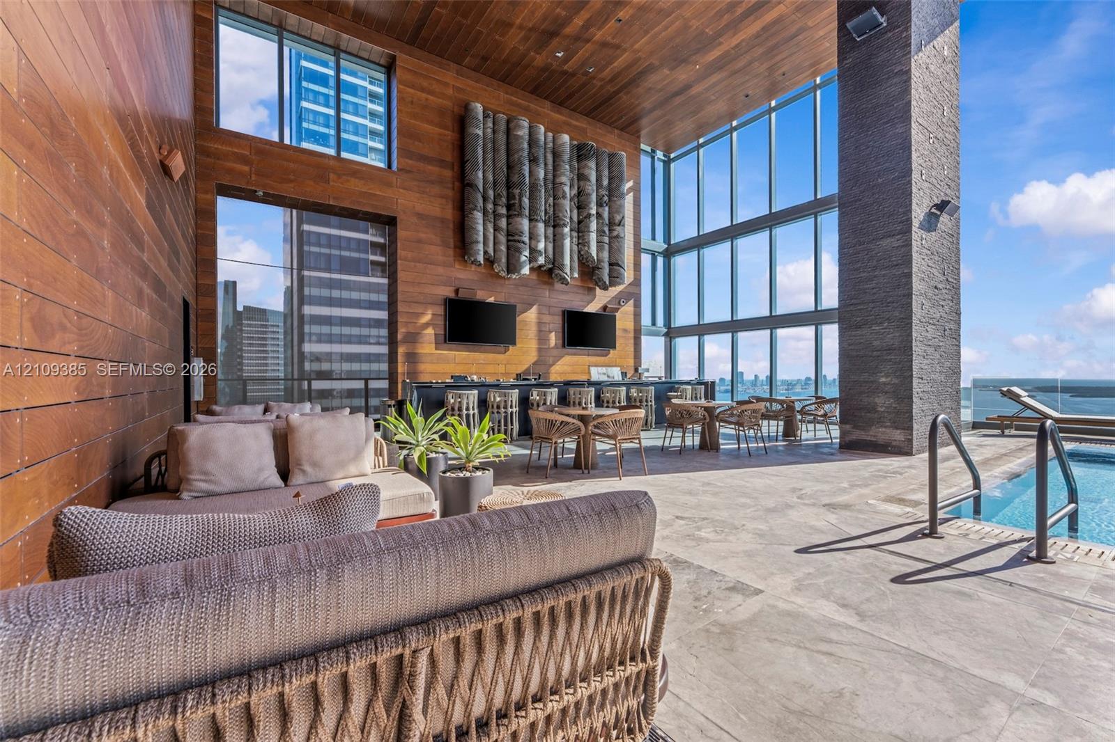 Outdoor lounge featuring wood-paneled walls and ceiling, floor-to-ceiling glass windows, stone-tiled flooring, and a recessed swimming pool with metal handrails