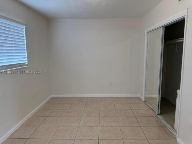 Interior room featuring neutral wall paint, tile flooring, horizontal window blinds, and a sliding mirrored closet door