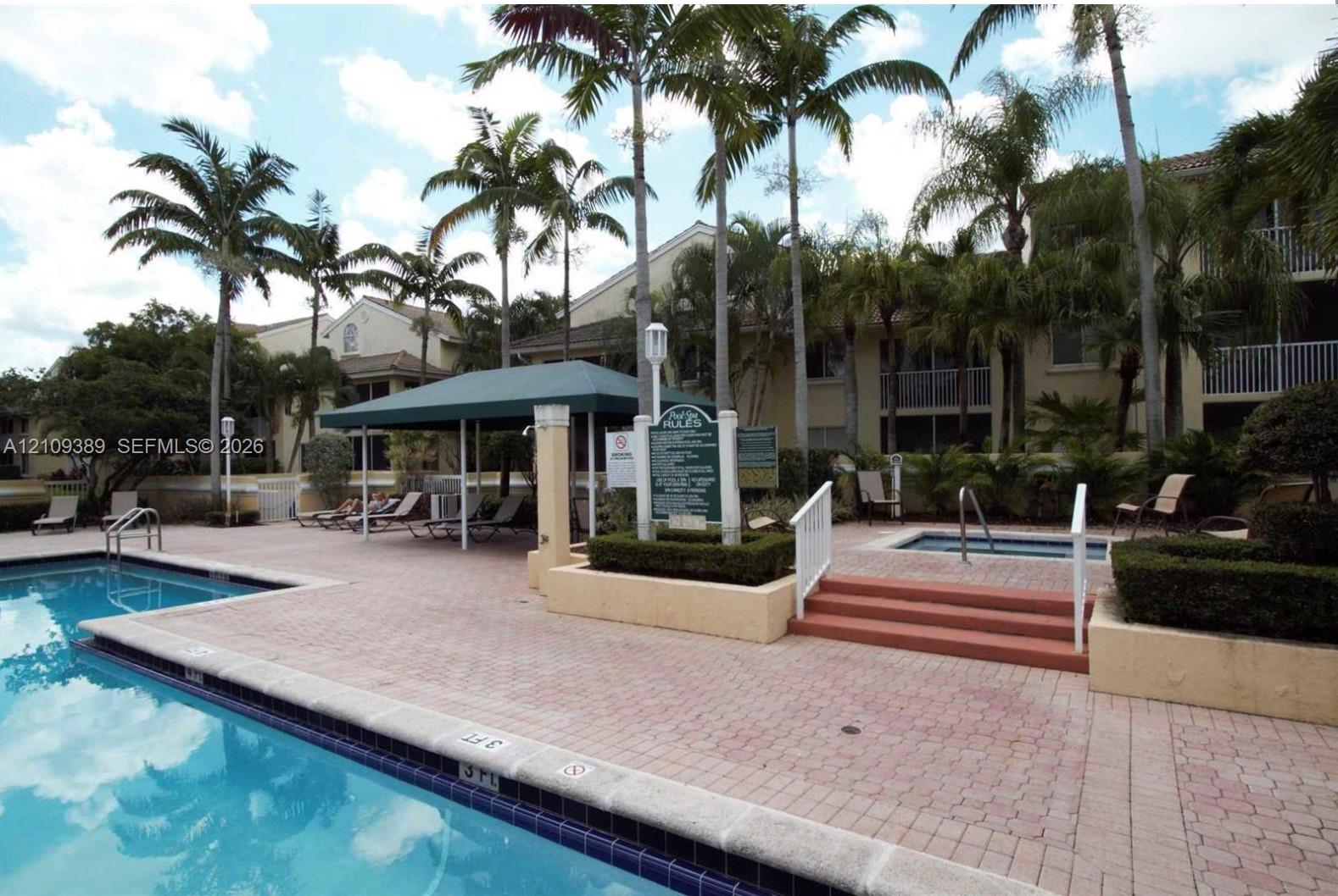 Community pool and spa area featuring brick paver decking, a covered seating structure, raised garden beds, and mature palm trees