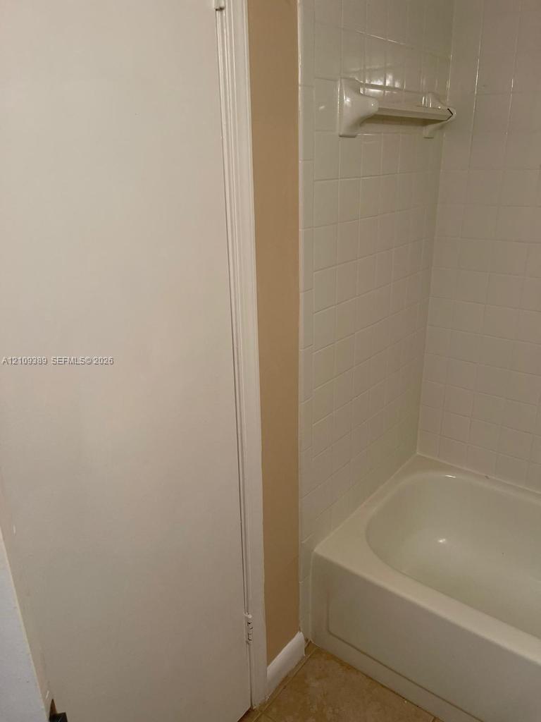 Bathtub featuring a white acrylic surround, wall-mounted white soap dish, and a built-in storage closet