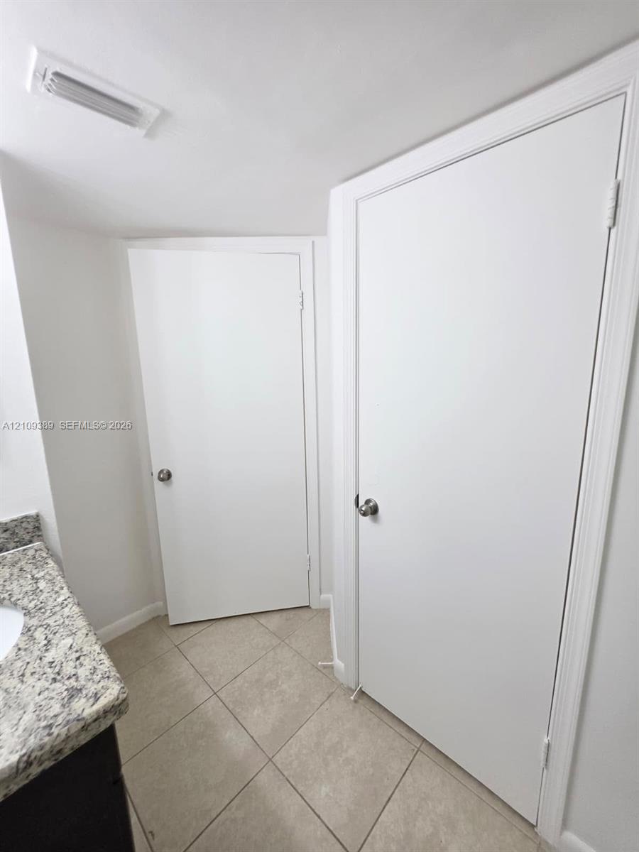 Stone-composite countertop with integrated sink and diagonal-set tile flooring, featuring two white interior doors with brushed metal hardware