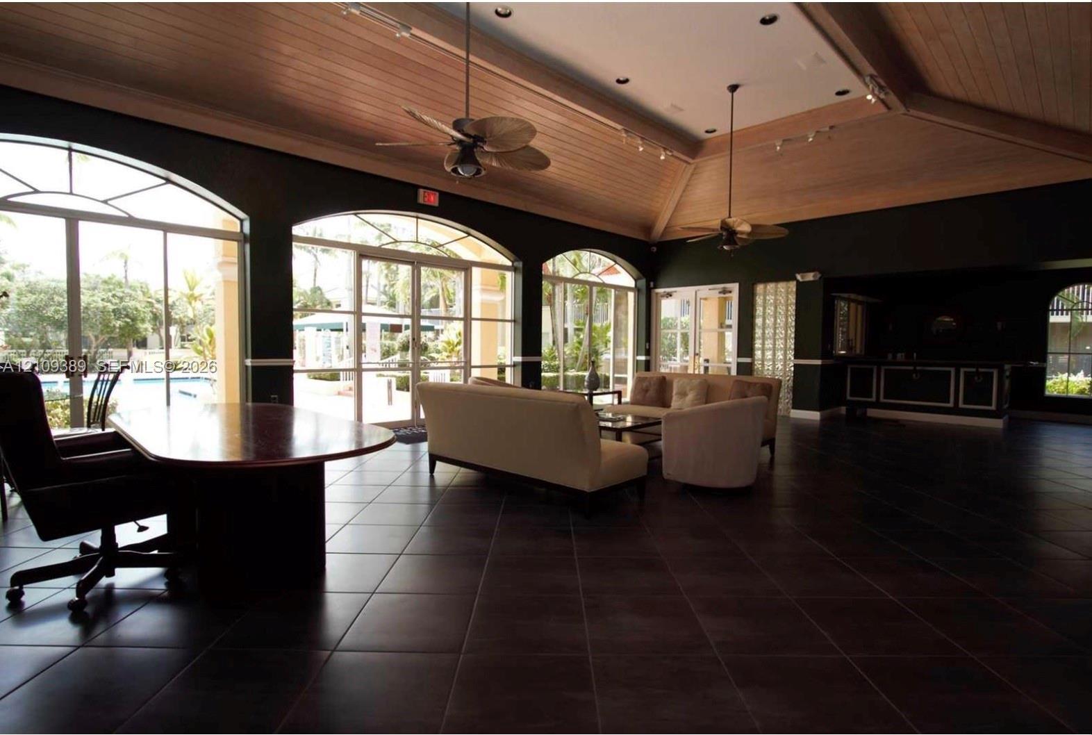 Vaulted wood-plank ceiling, large-format tile flooring, arched floor-to-ceiling windows, integrated recessed lighting, and ceiling fans