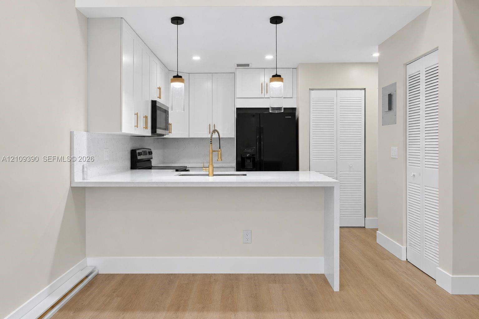 Kitchen featuring white shaker-style cabinetry, quartz countertops, a gold-toned pull-down faucet, dual glass pendant lights, and wood-finish flooring
