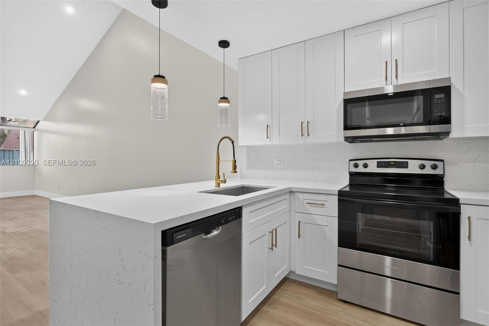 Kitchen featuring white shaker-style cabinetry, quartz countertops, stainless steel appliances, a brass-finish gooseneck faucet, and recessed pendant lighting