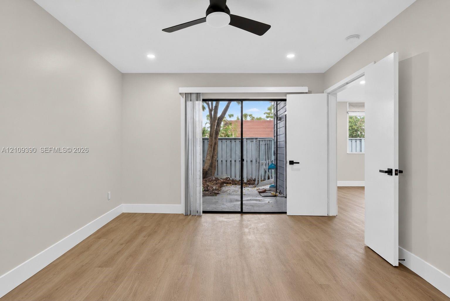Neutral-toned room featuring wood-finish flooring, a matte black ceiling fan, recessed lighting, and a sliding glass door providing external access