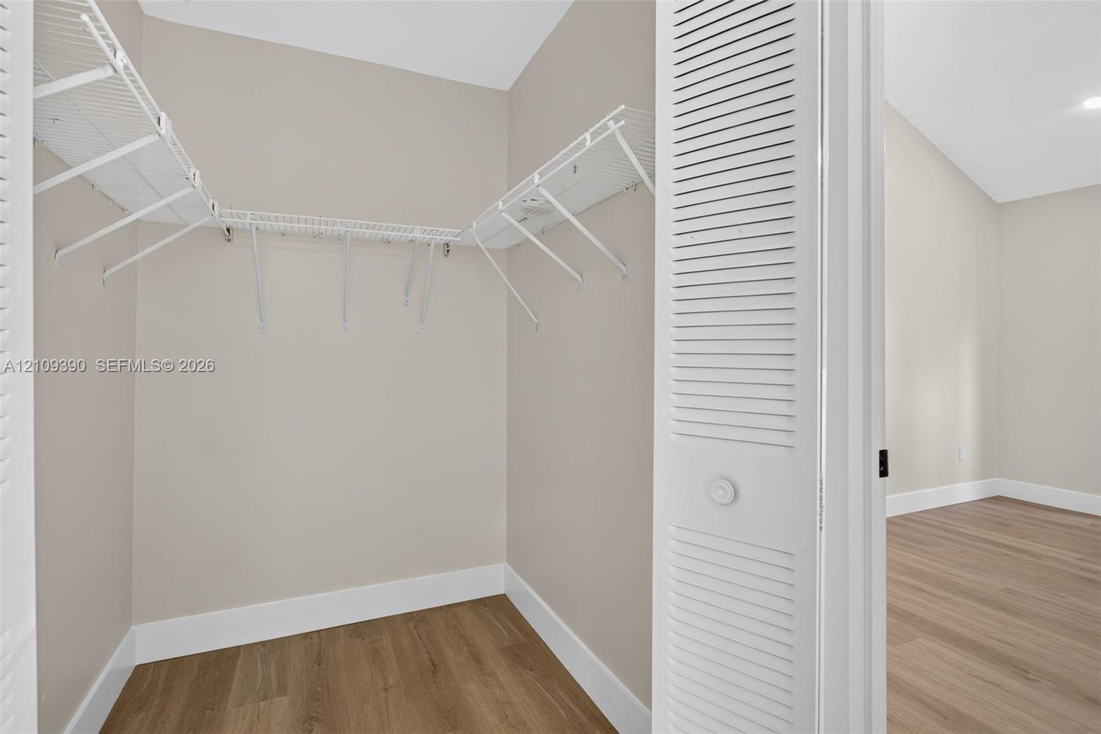 Walk-in closet featuring white wire shelving, wood-finish flooring, and white louvered bi-fold doors