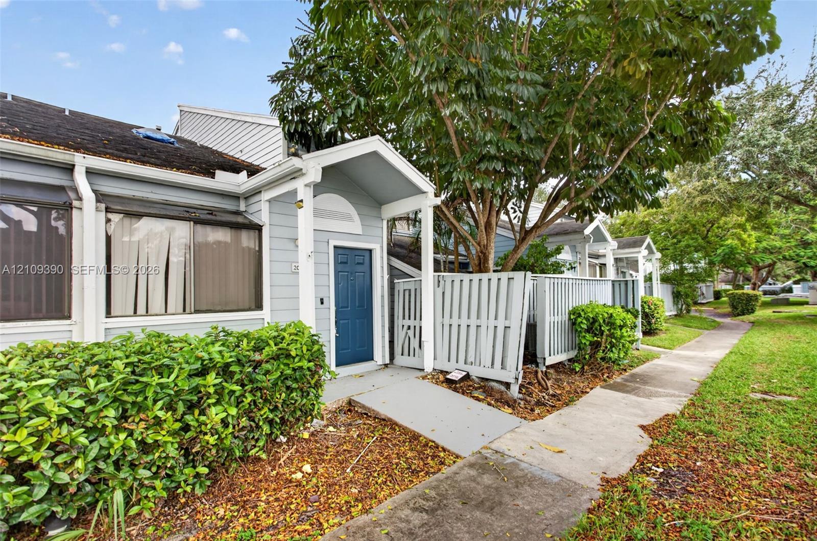 Light blue siding, covered entryway with gabled roof, blue paneled front door, and private fenced patio