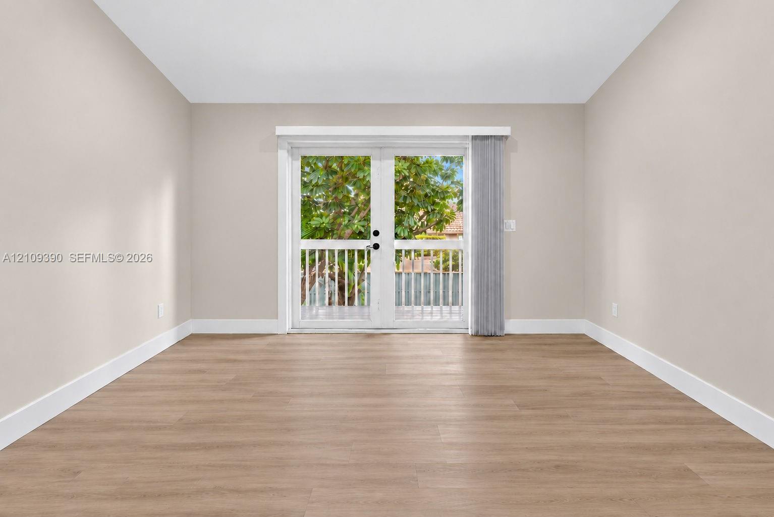 Neutral interior room featuring wood-finish flooring, white walls, and French doors opening to an exterior balcony
