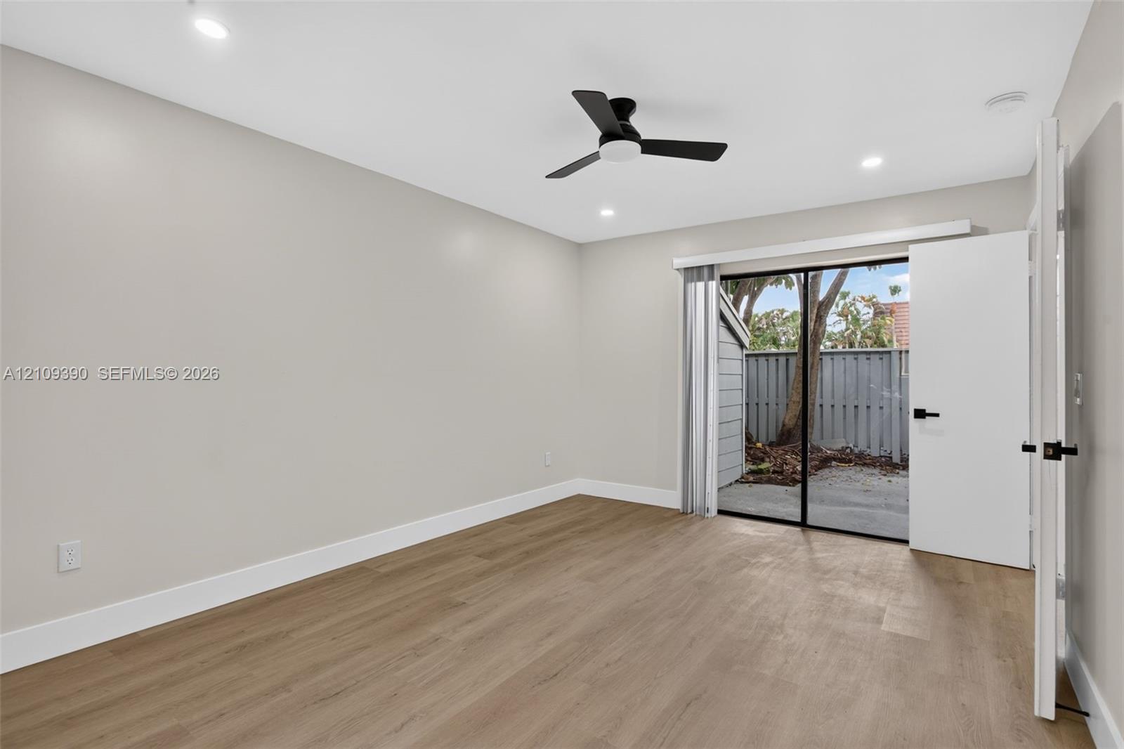 Neutral-toned interior featuring wood-finish flooring, recessed lighting, a matte black ceiling fan, and sliding glass doors with exterior access to a patio area
