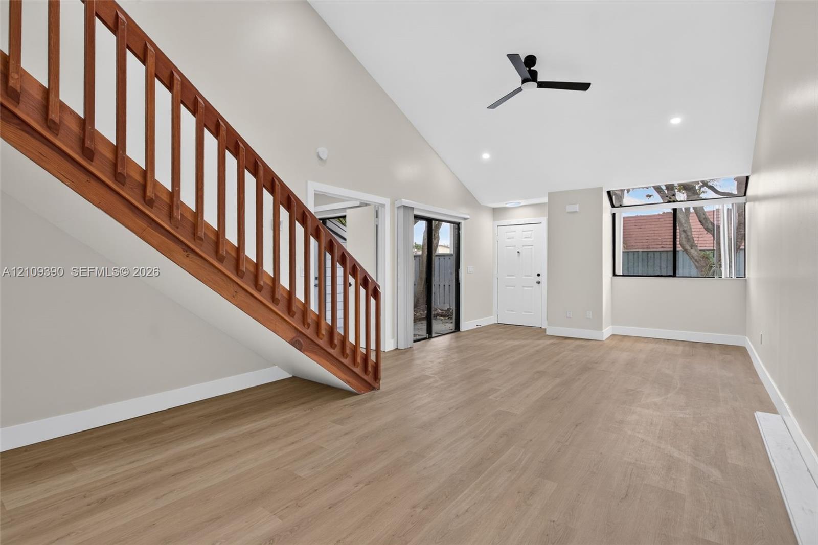 Vaulted ceilings with a ceiling fan, wood-finish flooring, and a wooden staircase railing