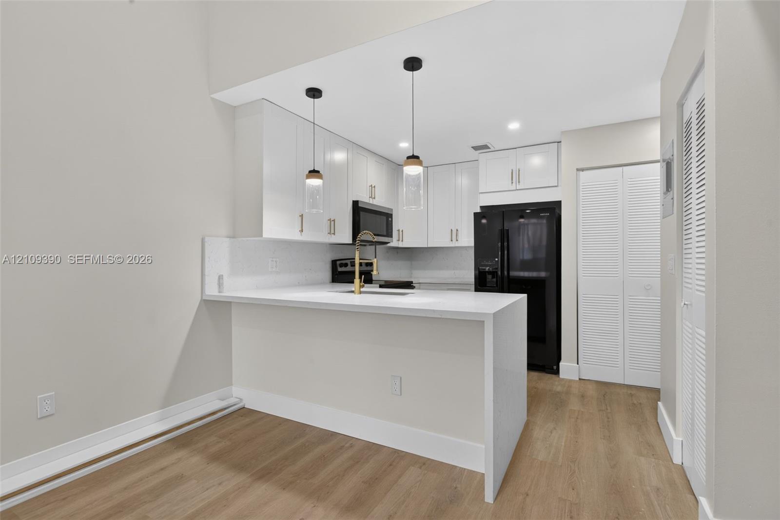 Kitchen featuring white shaker-style cabinetry, a quartz waterfall-edge peninsula, brass-finish faucet, pendant lighting, and wood-finish flooring