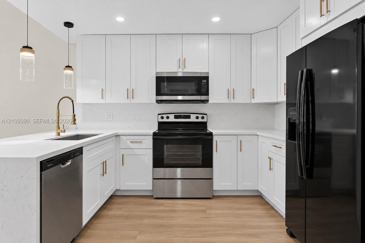 Kitchen featuring white Shaker-style cabinetry, quartz countertops, wood-finish flooring, gold-tone hardware, and two cylindrical glass pendant lights