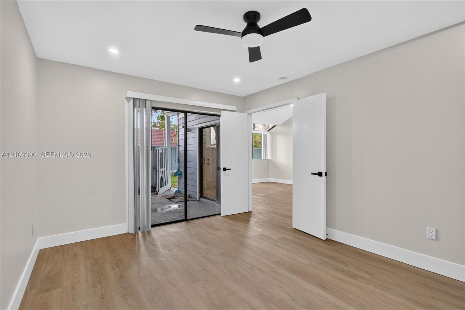 Room featuring wood-finish flooring, recessed lighting, a modern ceiling fan with integrated light, sliding glass doors, and dual-panel doors with matte black hardware