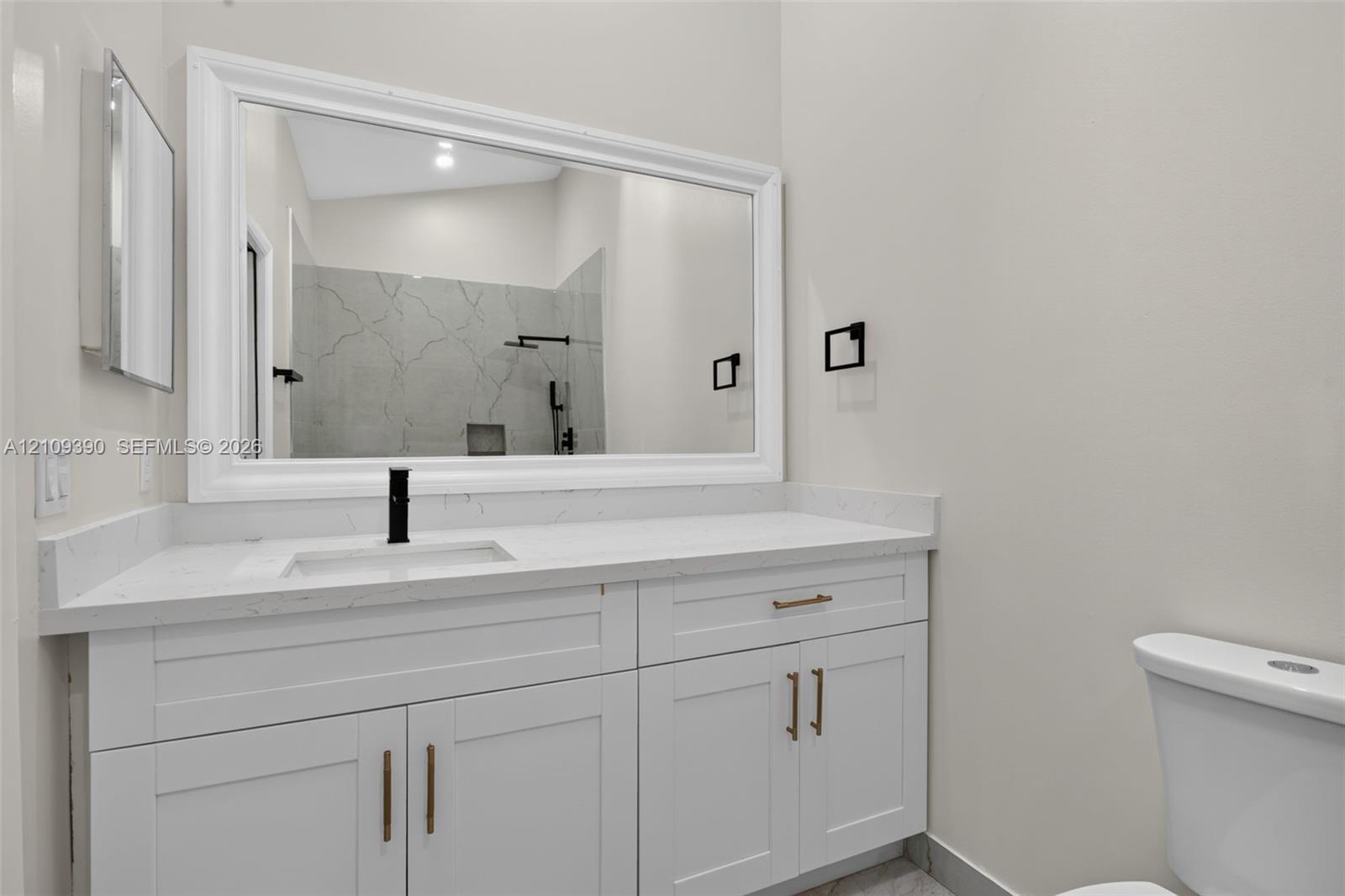 White cabinetry with brass-toned hardware, quartz countertop, undermount sink with matte black faucet, and framed vanity mirror