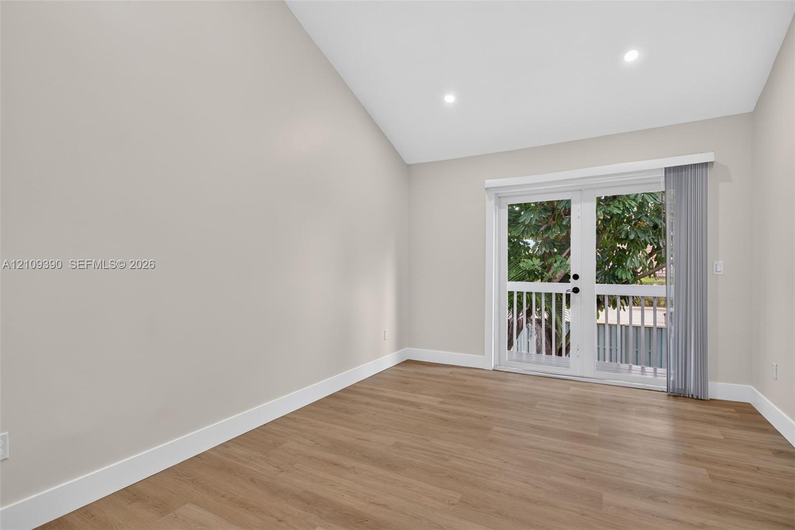 Vaulted ceilings, wood-finish flooring, recessed lighting, and double glass doors leading to an exterior balcony