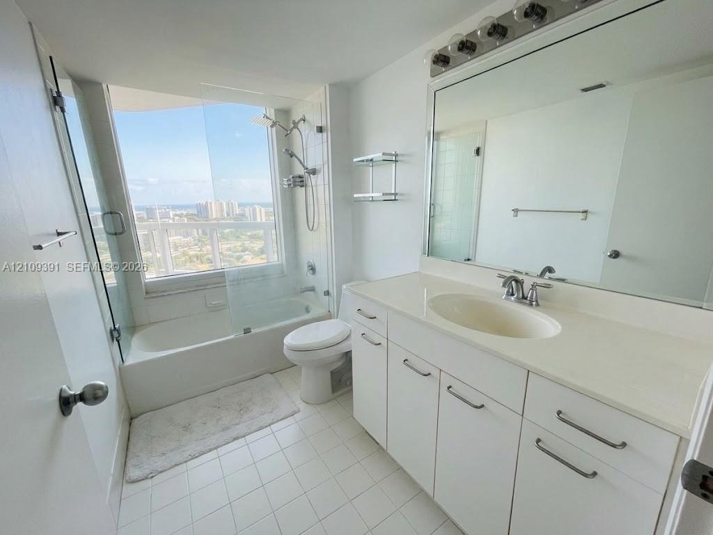 Bathroom featuring a white vanity with integrated countertop sink, full-width wall mirror, shower-tub combination with glass enclosure, and large-format window