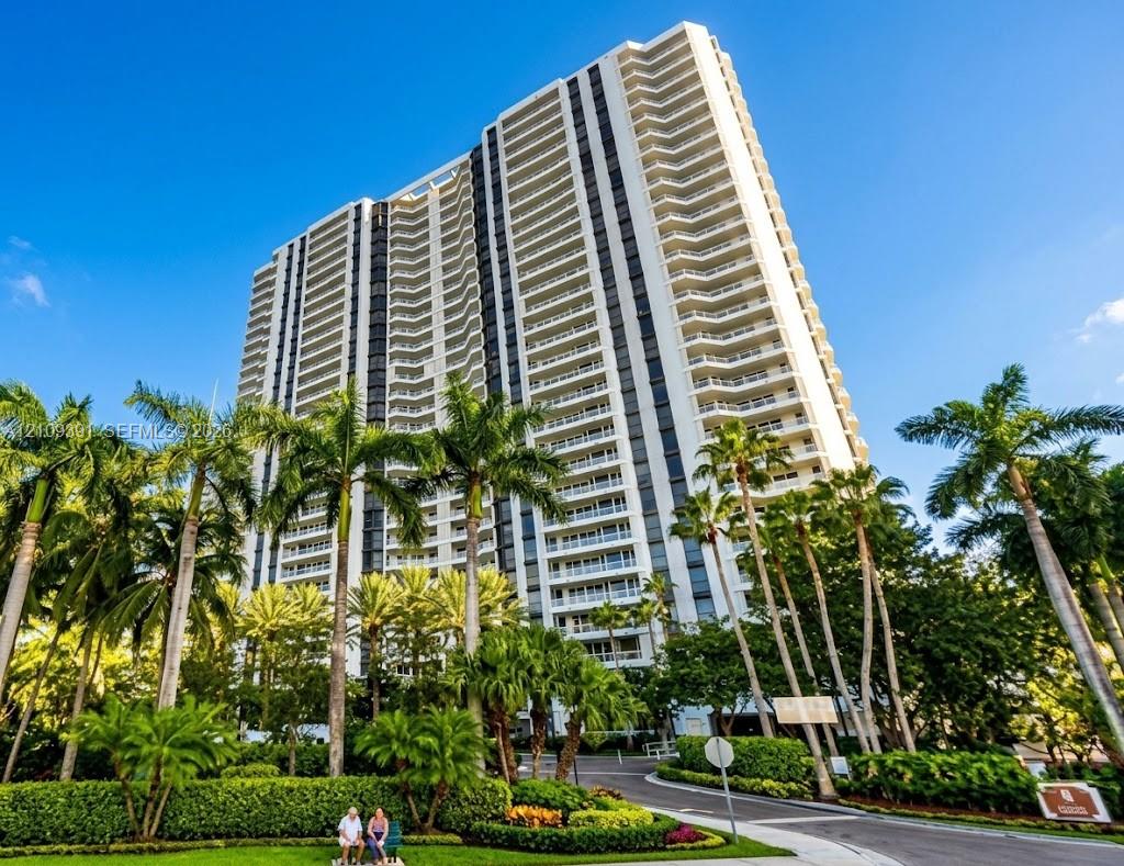 High-rise tower featuring multi-level private balconies, expansive glass windows, and a structured exterior facade, surrounded by established tropical landscaping High-rise tower featuring multi-level private balconies, expansive glass windows, and a structured exterior facade, surrounded by established tropical landscaping