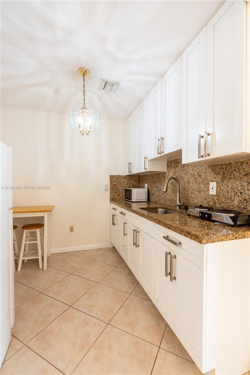 Kitchen featuring white shaker-style cabinetry, stone-finish countertops, stainless steel undermount sink with arched pull-down faucet, and neutral tile flooring