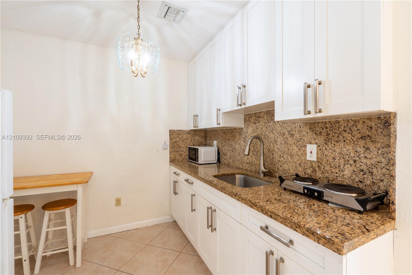 Kitchen featuring white cabinetry, stone-surface countertops, tile flooring, an undermount stainless steel sink with a pull-down faucet, and a decorative pendant light fixture