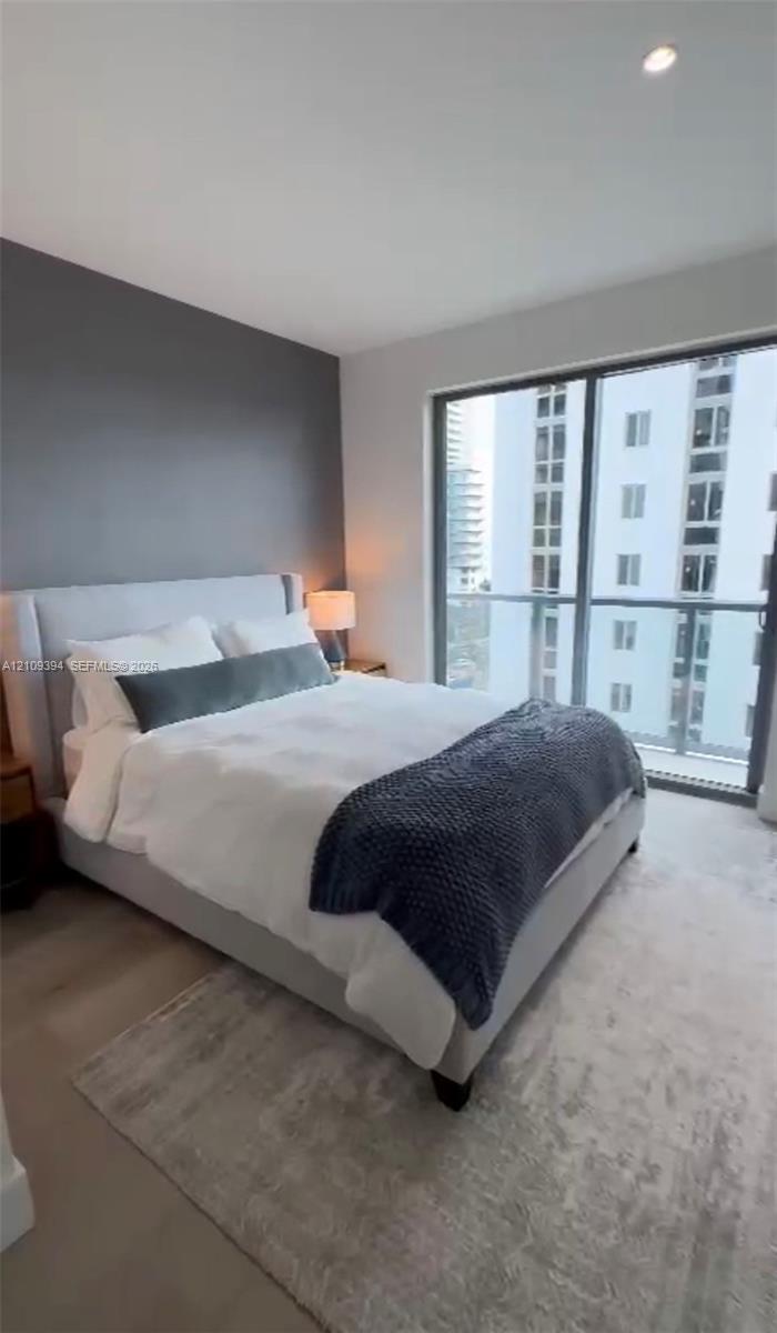 Floor-to-ceiling glass sliding doors, private balcony, accent wall, recessed ceiling lighting, and neutral-toned carpeting