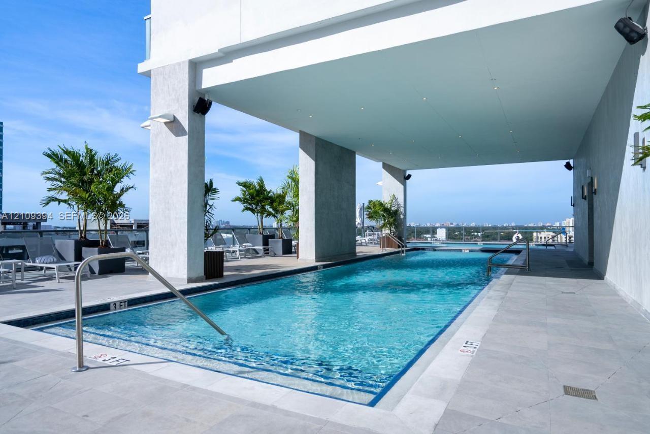 Rooftop swimming pool featuring stone tile decking, recessed lighting, architectural columns, and integrated handrails