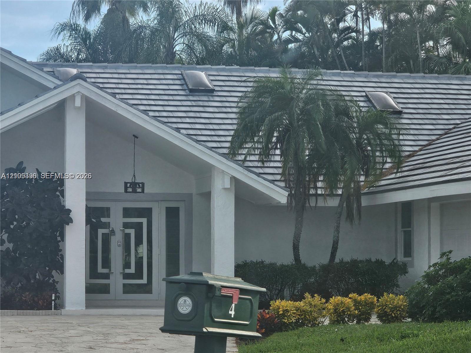 Exterior entrance featuring dual glass-panel doors with geometric detailing, gabled roofline, integrated skylights, and a covered portico with square structural columns