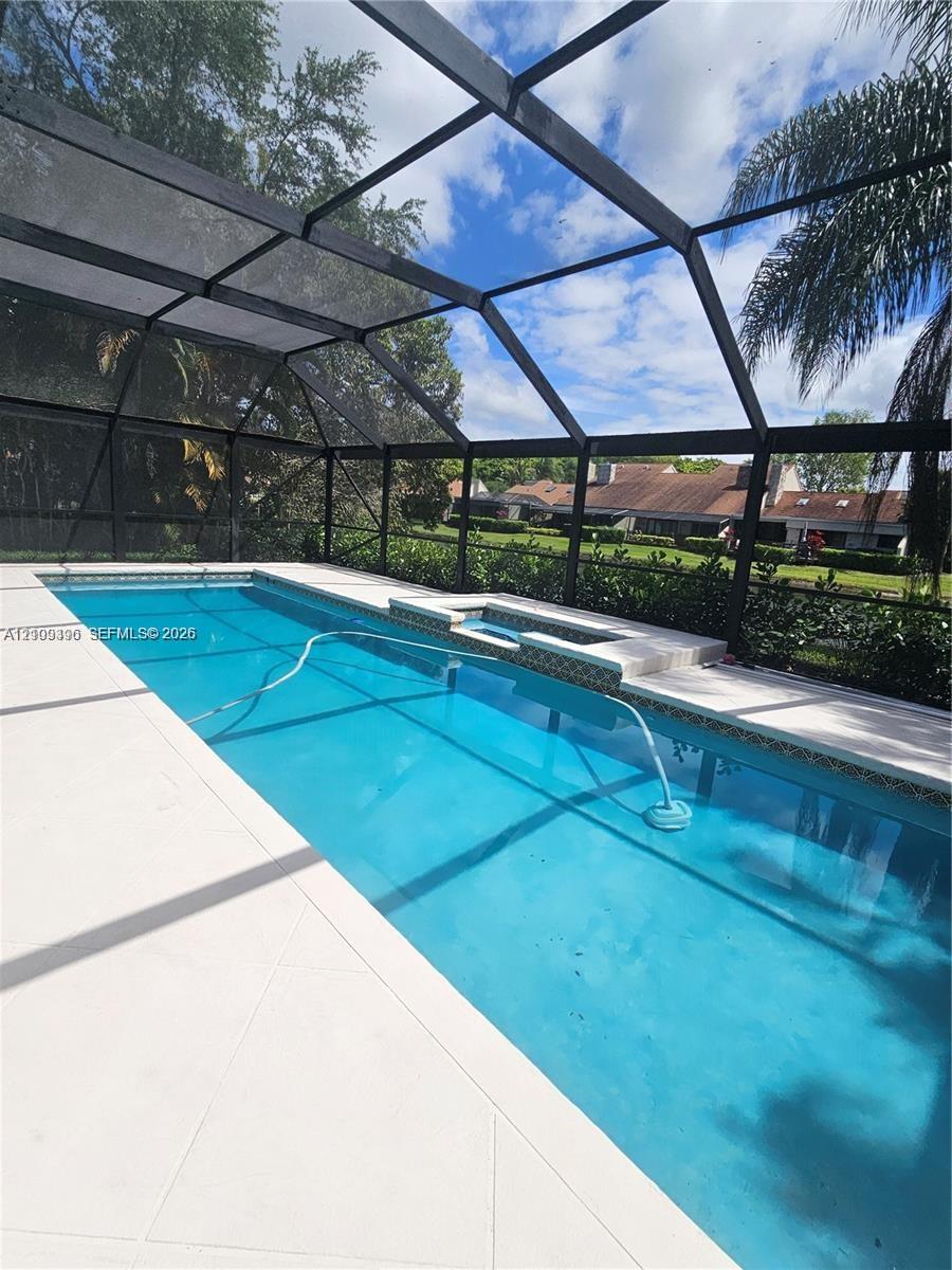 Screened pool enclosure with a geometric pool, integrated spa, tiled water line, and concrete pool deck