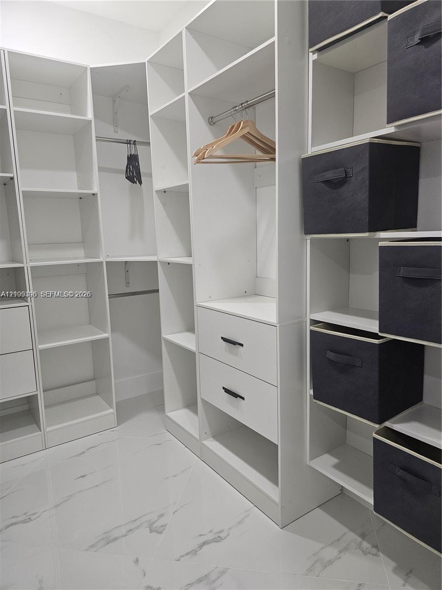 Custom reach-in closet featuring white floor-to-ceiling built-in shelving, integrated hanging rods, two soft-close drawers with matte black hardware, and polished stone-finish flooring