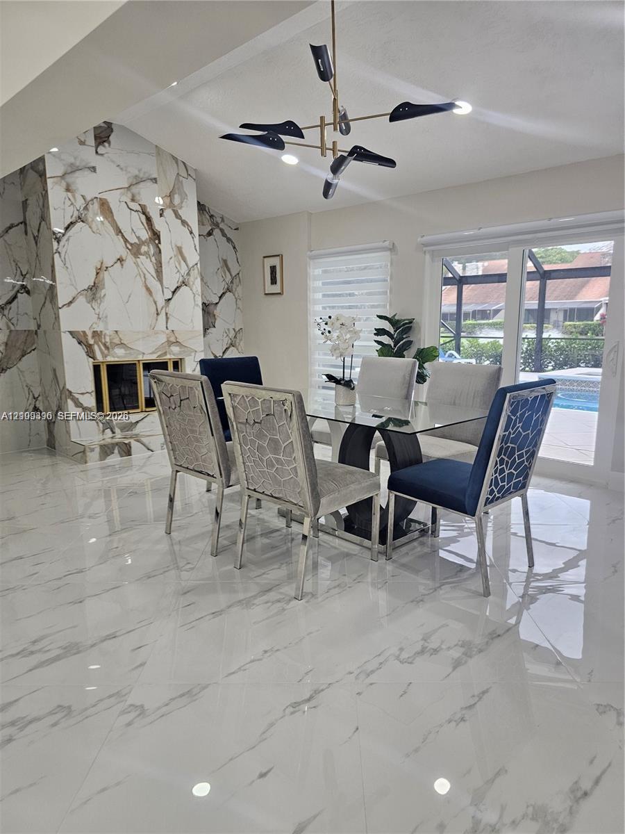 Floor-to-ceiling stone fireplace surround, polished large-format tile flooring, modern multi-arm chandelier, and sliding glass doors with access to an exterior screen enclosure
