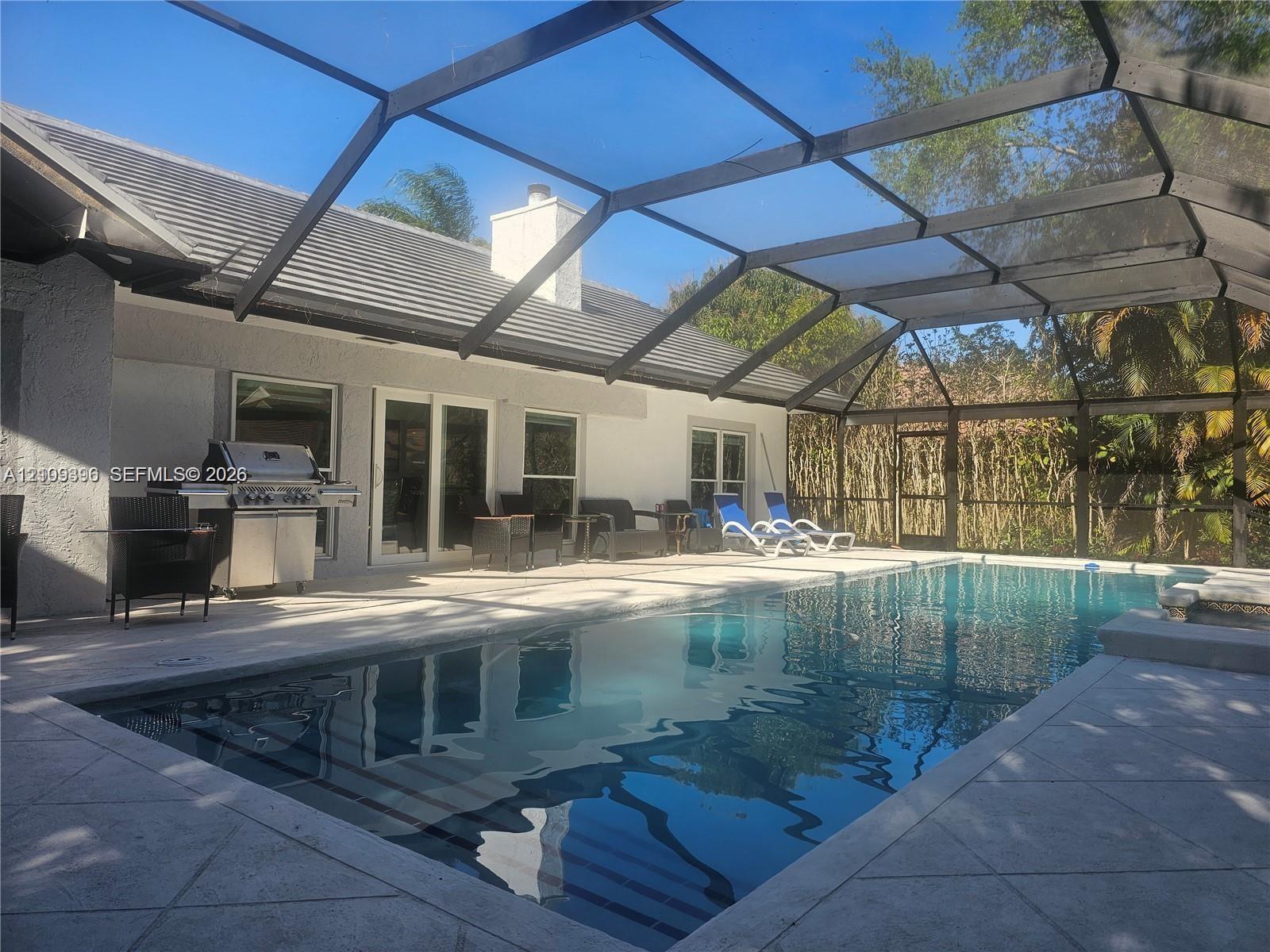 Screen-enclosed patio area featuring an inground pool, tiled deck, and built-in outdoor cooking station