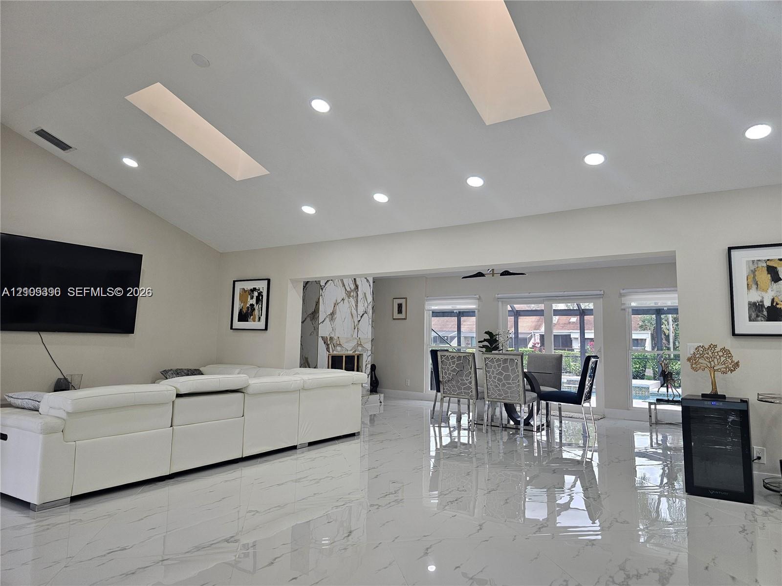 Vaulted ceilings featuring dual skylights, recessed lighting, polished stone-finish flooring, and a floor-to-ceiling stone-surround fireplace
