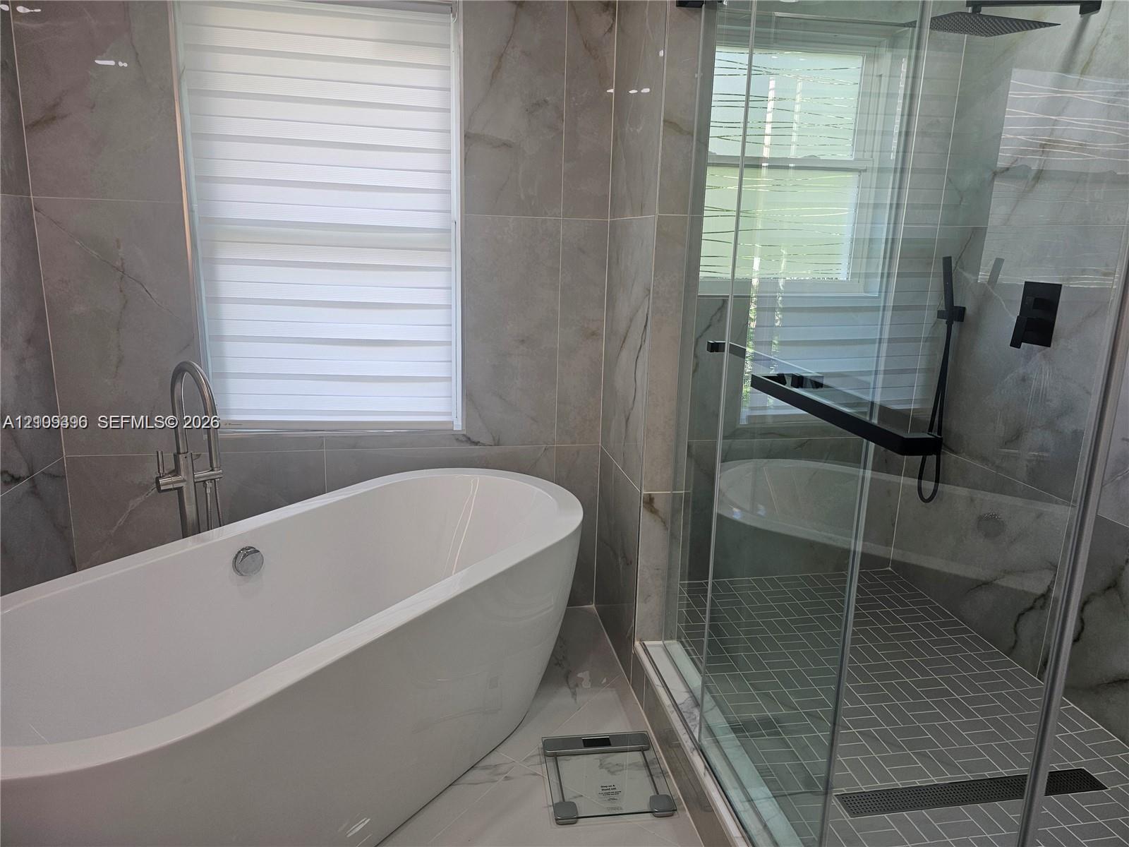 Freestanding oval soaking tub with floor-mounted faucet, walk-in glass-enclosed shower featuring a rainfall showerhead, and large-format wall tiling with a natural stone-pattern finish